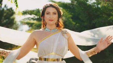 Ellerini çırpıp dua eden mutlu, fantezi kadını. Beyaz ipek uzun elbiseler rüzgarda uçar altın mücevherler taç diyabet kolye geniş bilezikler metal kemer. Seksi kız, eski Yunan tarzı. Gün ışığı 4k