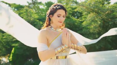 Fantezi mutlu kadın gözleri dua ederken kapalı. Beyaz ipek uzun elbiseler rüzgarda uçar altın mücevherler taç diyabet kolye geniş bilezikler metal kemer. Seksi kız, eski Yunan tarzı. Gün ışığı 4k