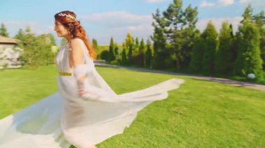 Neşeli, güler yüzlü, fantezi kadın Yunan tanrıçası dans ediyor uzun, ipek, beyaz elbiseler havada uçuşuyor. Neşeli peri kız gelin gülümseyen surat. Gün ışığı yeşil park