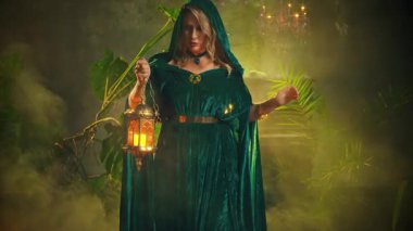 Sanat portresi, mistik kadın kraliçesi elinde fener lambasıyla gecenin karanlığında yürüyor. Pelerinli gotik kız kafasında yeşil kapüşon, sihirli mumlar video 4k