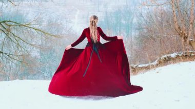 Dağın tepesinde dans eden mutlu bir kadın. Eteği elinde tutan, kırmızı kumaşı rüzgarda dalgalanan bir kadın. Prenses kız kışın tadını çıkarıyor. Taze, soğuk, beyaz kar. Arka taraftaki bayan sanat 4k