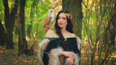 Sanat portresi Fantezi kadın tanrıça elf, beyaz evcil kuş baykuş ahır baykuşu omuzunda oturuyor. Yeşil sarı orman ağaçları sihirli güneş ışığı. Yeşil elbiseli kürk pelerini Yunan tarzı altın çelenk. Yaz doğası.