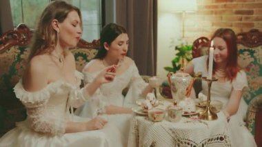Kek yiyen bir kadın çay kaşığıyla çay fincanı üzerinde kek yiyor sıcak çay fincanı seti içiyor. Kanepede oturan asil bayan kahve masası kızı oturma odasında dinleniyor beyaz eski moda elbise eski usul akşam yemeği.