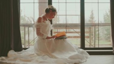 Seksi kadın prenses, kitap okuyor. El ele tutuşup pencere kenarında oturuyor. Yetişkin kız rüyasında güzel dudaklar kraliyet odasında dinleniyor. Bayan Kraliçe Beyaz Vintage elbise Uzun eski tarz sarı saç 4K.