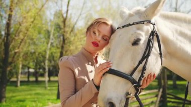 Güzel, güzel, gülümseyen yüz, kırmızı dudaklar, beyaz elli, at kürküne dokunan mutlu kadın, sanat portresi, at evcil hayvanı. Mutlu seksi kız eski moda kıyafetler sihirli güneş ışığı ağacı 4k