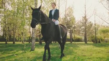 Zarif genç kadın ata biniyor, asil bayan eski tarz kıyafetler yeşil çimlerin tadını çıkarıyor doğa güneş ışığı gökyüzünü aydınlatıyor. Fantezi prensesi kız jokey at sırtında oturur dizginleri tutar