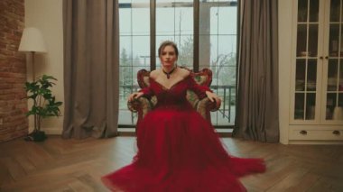 Sanat portresi fantezi kraliçesi tahttan kalkar, ortaçağ bayanı uzun kırmızı elbiseli Gotik taç giyer. Kraliyet lüksü klasik beyaz oda penceresi ışığı. Seksi prenses kız. Şeytani peri masalı eski usul.