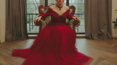 Sanat fantezi kraliçesi eski tarz tahttan kalkıyor. Uzun, gür kırmızı elbise. Kraliyet sandalyesi klasik beyaz oda penceresi ışığı. Seksi Prenses Masalı Gotik Bayan Nedime 4k