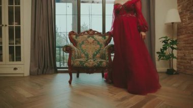 Sanat kraliçesi eski tarz bir tahtta oturur. Uzun, lüks kırmızı elbise etek etek balo elbisesi. Kraliyet sandalyesi beyaz oda penceresi. Seksi prenses kız peri masalı güzeli surat. Karnaval temalı parti.