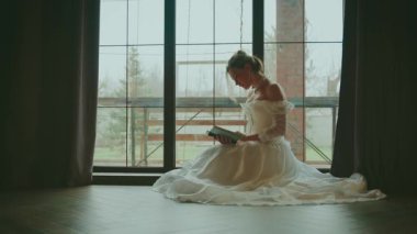Karanlık gölge, siluet, kitap okuyan seksi kadın. El ele tutuşup pencerenin kenarında oturuyor. Yetişkin bir kız güzel bir yüz hayal eder. Kraliyet odasında dinlenin. Beyaz kaliteli elbise. Uzun balo elbisesi, eski tarz 4K.
