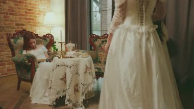 Mutlu kadın kraliçe ve arkadaş baş nedimeler iletişim kurar. Soylu bayan prenses kanepede oturuyor ve kraliyet ailesinde birlikte çay partisi veriyor. Beyaz balo elbisesi eski moda.