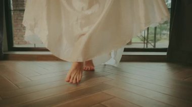 Yakın çekim çıplak ayaklı kadın ayakları parke zeminde yürüyor, Fransız ringa kemikli meşe ağacından yapılmış gibi duruyor. Klasik bayan çıplak ayakla evde rahat rahat dolaşıyor. Kadın bacakları uzun beyaz elbise