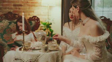 Mutlu kadın şeker kasesini elinde tutuyor. Karışık şekeri çay kaşığıyla çay fincanının içine koyuyor. Kanepede oturan asil kadın kahve masası kızı oturma odasında dinleniyor beyaz eski tarz elbise 4K