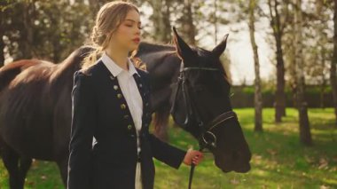 Güzel yüzlü, geçmişe dönük, mutlu, atıyla yürüyen kadın. Parlak güneş ışığı yeşil çimen orman parkı ağacını aydınlatıyor. Jokey giysili kız prenses eski usul para, dizginler siyah at. Aşkım.