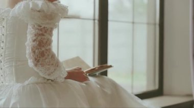 Genç, seksi Victoria 'lı kadın. El ele kitap okuyor. Pencere kenarında oturuyor. Seksi yetişkin kız, kraliyet odasında dinleniyor. Beyaz, klasik, uzun balo elbisesi, eski moda dikiz aynası. Naiplik çağı