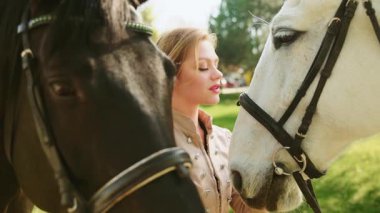 Manken pozu veren güzel, mutlu, fantezi kraliçesi, at gibi seksi, gülümseyen iki at, siyah kahverengi ve beyaz hayvan ağızlık takıyor. Aşk evcil hayvanı. Eski moda takım elbise. Eski moda sanat 4K.