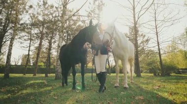 At mankeni pozu veren güzel yüzlü fantezi kadın. Mutlu Jokey kız ahırda iki atı dizginliyor siyah ve beyaz hayvan. Aşk evcil hayvanı. Yaz doğası güneş ışığı 4k ışık saçıyor.