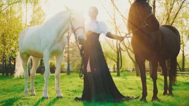 Atlı fantezi kraliçesi. Mutlu yetişkin kız güzel surat. İki atı tutan kadın siyah beyaz bir hayvan. Aşk evcil hayvanı. Yaz doğası güneş ışığı parlıyor. Eski tarz elbise, 4k video klibi..