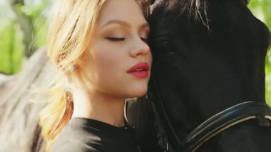 Yakın plan güzellik, kırmızı dudaklar mavi gözler at eli ile mutlu kadın ağızlık siyah kürke dokunuyor dostluk bakımı at hayvanı. Şık seksi kız eşofmanı siyah elbise. Sihirli güneş ışığı ağacı 4k