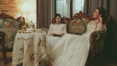 Kadınlar, ellerinde kitap okuyarak can sıkıntısından ölüyorlar. Sarışın kadın asil bayan güzel yüz dudakları. İki kadın kanepede dinlenir kraliyet odası beyaz eski moda elbise.