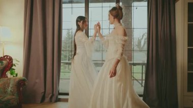 İki mutlu kadın klasik odada dans edip neşe saçan gülen yüzler takınıyorlar. Peri masalı gelin yetişkin kızlar güzel asil kadın. Kraliyet evi beyaz eski moda elbise uzun balo elbisesi eski tarz parti