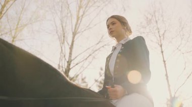 Zarif, mutlu genç bir kadın ata biniyor, soylu bayan yaşlı para tarzı kıyafetler yürümeyi seviyor kutsal güneş ışınları gökyüzünü aydınlatıyor. Fantezi ergen kız jokey at sırtında oturur dizginleri tutarak 4k.