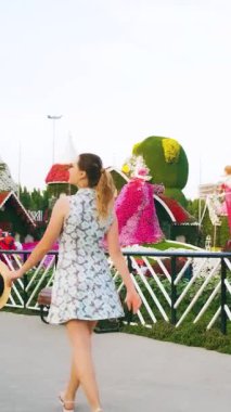 Neşeli, mutlu, güzel, genç bir turist sokak bahçesinin önünden geçiyor. Yetişkin bir kız dans ediyor. Güzellik manzarasına bayılıyor. Renkli çiçekler. Hasır şapka. dikey video