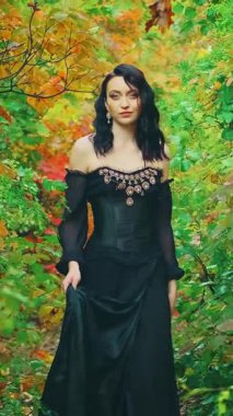 Siyah gotik kıyafet yürüyüşleri içinde kraliçe fantezi kadın, sonbahar doğa ağaçları. Yeşil sarı turuncu yeşillik parkı. Prenses kız seksi manken. Kraliyet vintage uzun siyah balo elbisesi. video 4k