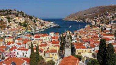 Symi (Simi) ada limanı, klasik gemi yatları, ada tepelerindeki evler, Ege Körfezi manzarası. Yunanistan adaları Rodos adasından tatil turları düzenliyor. Symi, Yunanistan, Dodecanese.