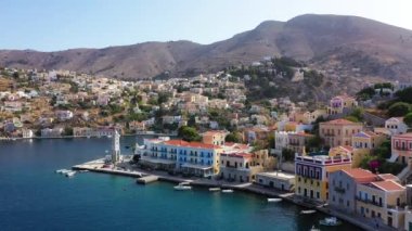 Symi (Simi) ada limanı, klasik gemi yatları, ada tepelerindeki evler, Ege Körfezi manzarası. Yunanistan adaları Rodos adasından tatil turları düzenliyor. Symi, Yunanistan, Dodecanese.