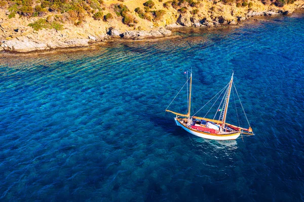 Aerial view of anchored sailing yacht in emerald sea. Aerial view of a boat. Outdoor water sports, yachting. Aerial view of anchoring yacht in open water. Ocean and sea travel and transportation