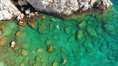 Mercan resifi üzerinde şnorkelle yüzen genç bir çiftin hava görüntüsü, kristal berrak suyun daha derin kısımlarına, Rodos, Yunanistan 'a ulaşıyor. Kristal berrak suda yüzen bir çiftin hava aracı görüntüsü..