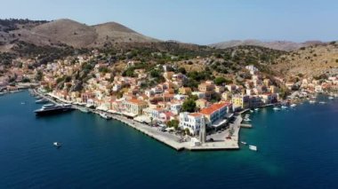Symi (Simi) ada limanı, klasik gemi yatları, ada tepelerindeki evler, Ege Körfezi manzarası. Yunanistan adaları Rodos adasından tatil turları düzenliyor. Symi, Yunanistan, Dodecanese.