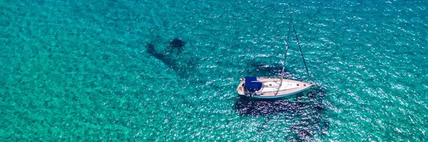 熱帯の島の前で透明なターコイズブルーの水の中でヨットの停泊 代替ライフスタイル ボートに住んでいます ターコイズブルーの水の上のアンカーでヨットの空中ビューは 豪華さ 富を示しています — ストック写真