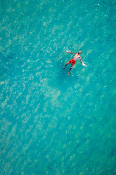 熱帯の海の水に浮かんでいる男のドローンビュー 熱帯の目的地で日光浴や休暇を楽しむ海の水に浮かぶ若い男の空中ビュー 人々は観光休暇の概念を旅行 — ストック写真