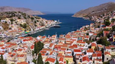 Symi (Simi) ada limanı, klasik gemi yatları, ada tepelerindeki evler, Ege Körfezi manzarası. Yunanistan adaları Rodos adasından tatil turları düzenliyor. Symi, Yunanistan, Dodecanese.