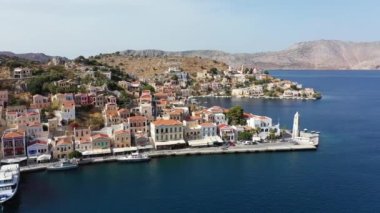 Symi (Simi) ada limanı, klasik gemi yatları, ada tepelerindeki evler, Ege Körfezi manzarası. Yunanistan adaları Rodos adasından tatil turları düzenliyor. Symi, Yunanistan, Dodecanese.