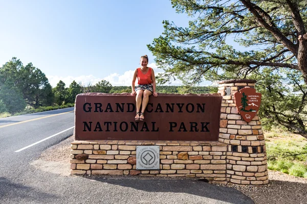 Κορίτσι που κάθεται στο εθνικό πάρκο Grand Canyon πινακίδα εισόδου — Φωτογραφία Αρχείου