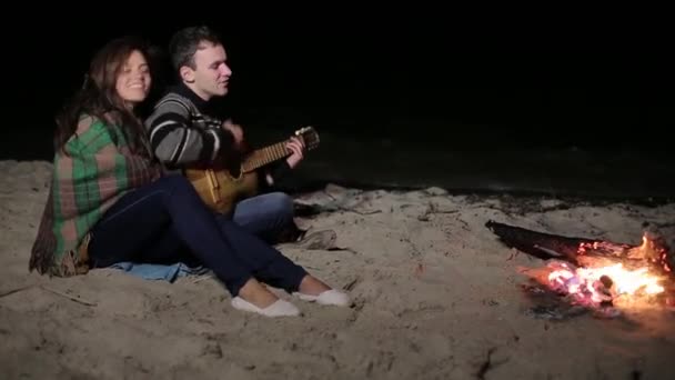 Человек играет на гитаре у огня и моря — стоковое видео