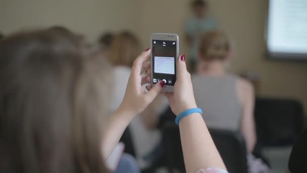 Девушка делает фото на смартфоне во время конференции — стоковое видео