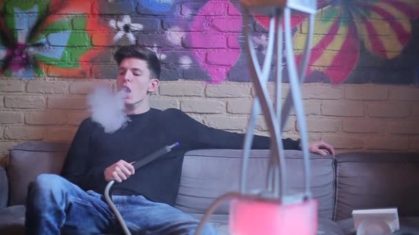 Brunette man smokes a hookah and let smoke rings — Stock Video