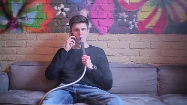 Brunette man smokes a hookah and talking on cell phone — Stock Video