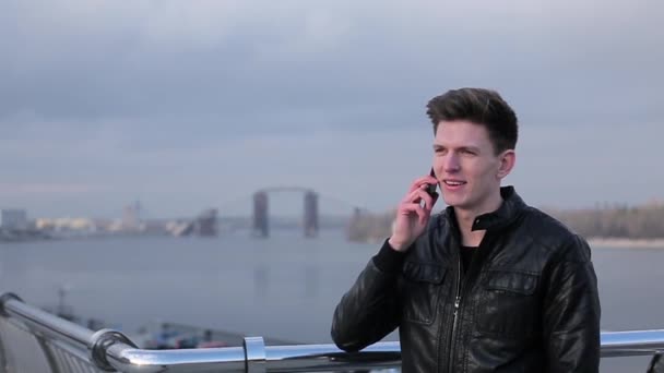 Brunette man praten op mobiele telefoon op een achtergrond van de stedelijke rivier — Stockvideo