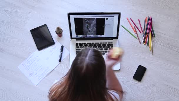 Meisje op zoek foto's op de laptop en eten apple — Stockvideo