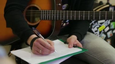 Adam bir akustik gitar akorları bir sayfada yazıyor.