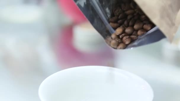 Granos de café derramados de la bolsa en una taza blanca — Vídeos de Stock