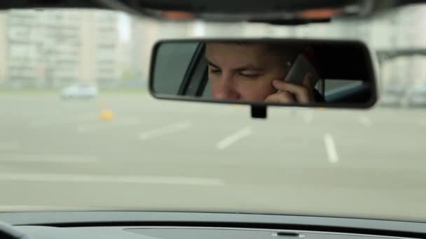 Мужчина разговаривает по телефону в зеркале машины — стоковое видео
