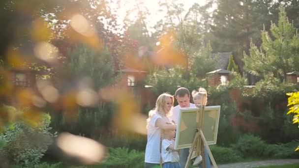 Junge Familie malt auf Staffelei im Garten — Stockvideo
