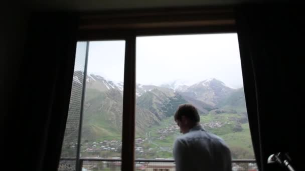 Homme debout devant une fenêtre sur un fond de montagne — Video