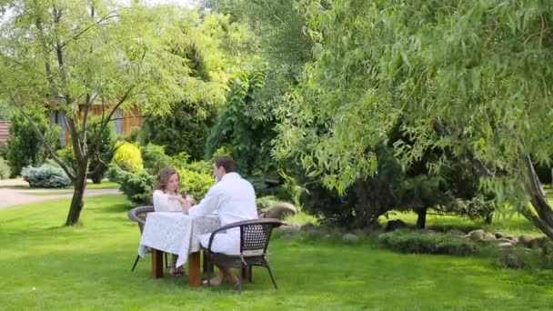 Pareja en las batas blancas desayunan en el jardín — Vídeos de Stock